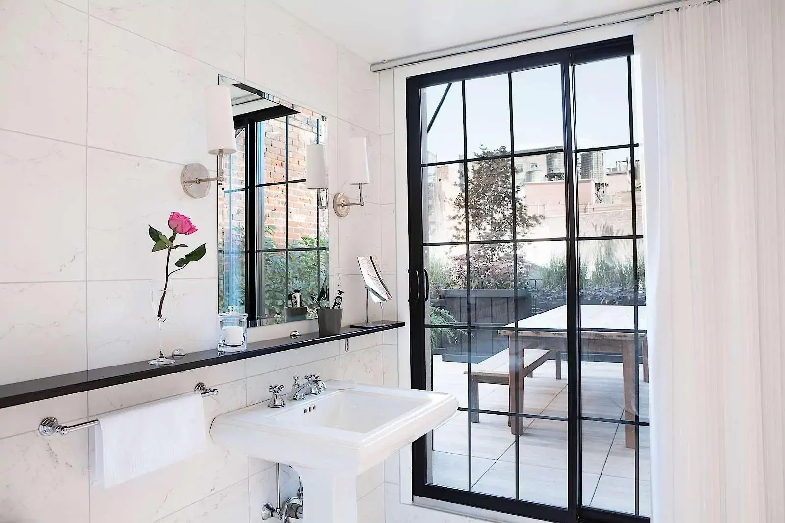 A white tiled hotel bathroom with a french door giving into a terrace