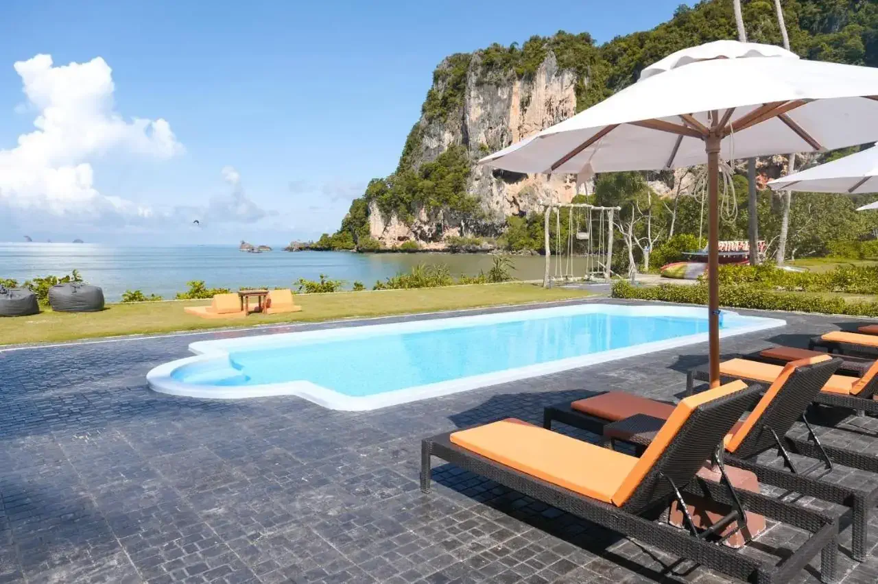 A pool with sun loungers by a beach surrounded by boulders on a sunny day