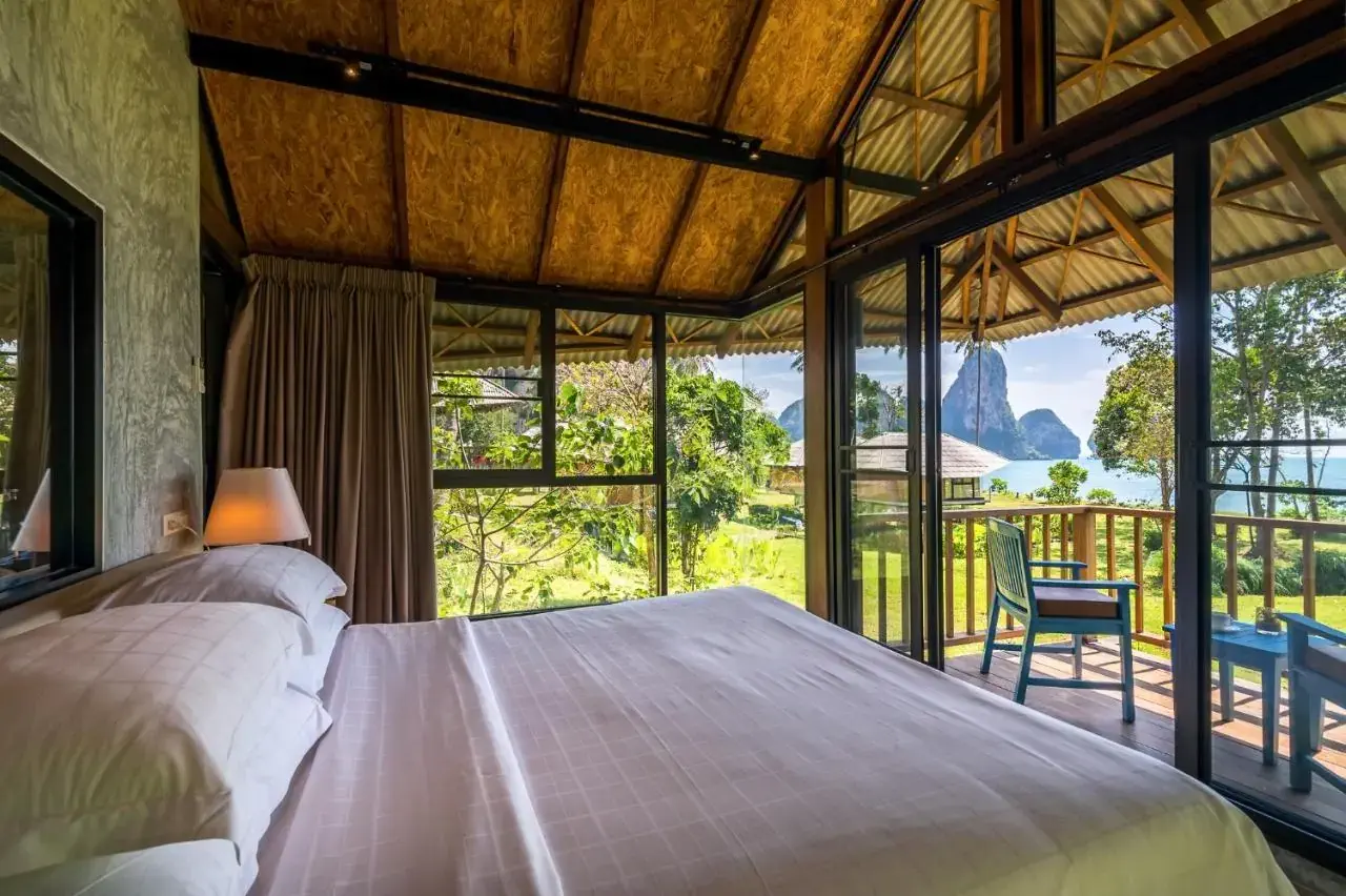 A bedroom in a hotel with palapa roof with views over a lawn and a tropical bay