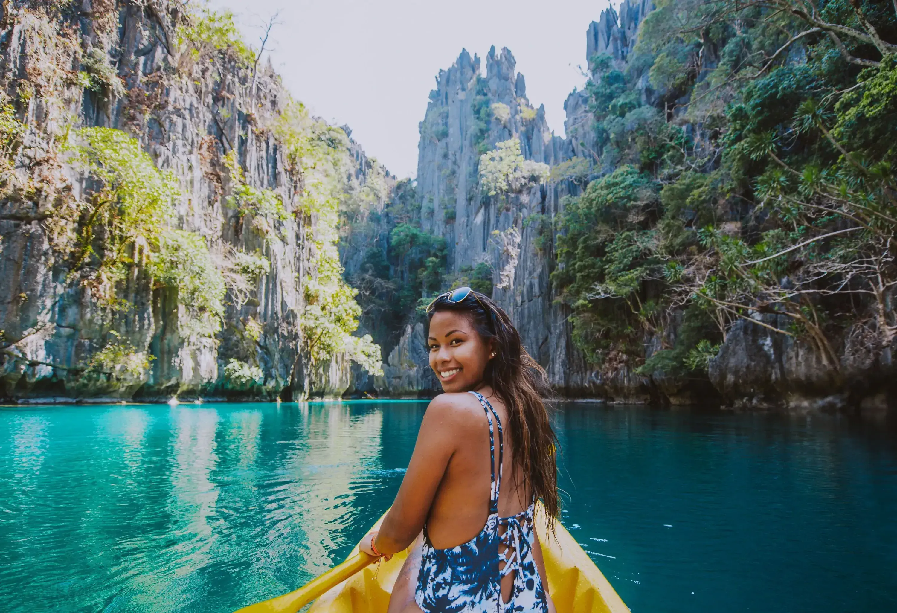 A person in a kayak facing backward with a joyful smile, set against the breathtaking backdrop of towering rock formations.