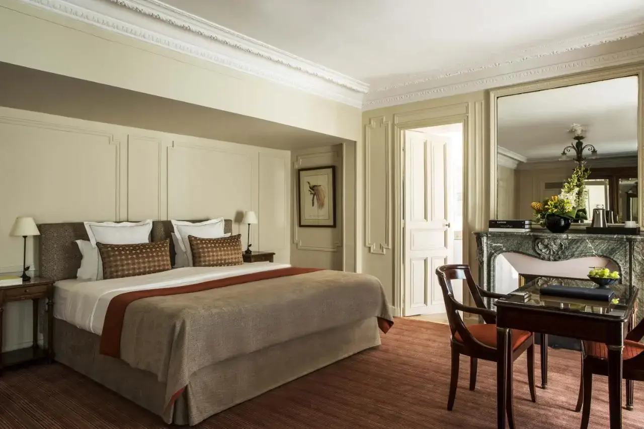 A large classic French hotel room with a bed and table with chairs by two French windows
