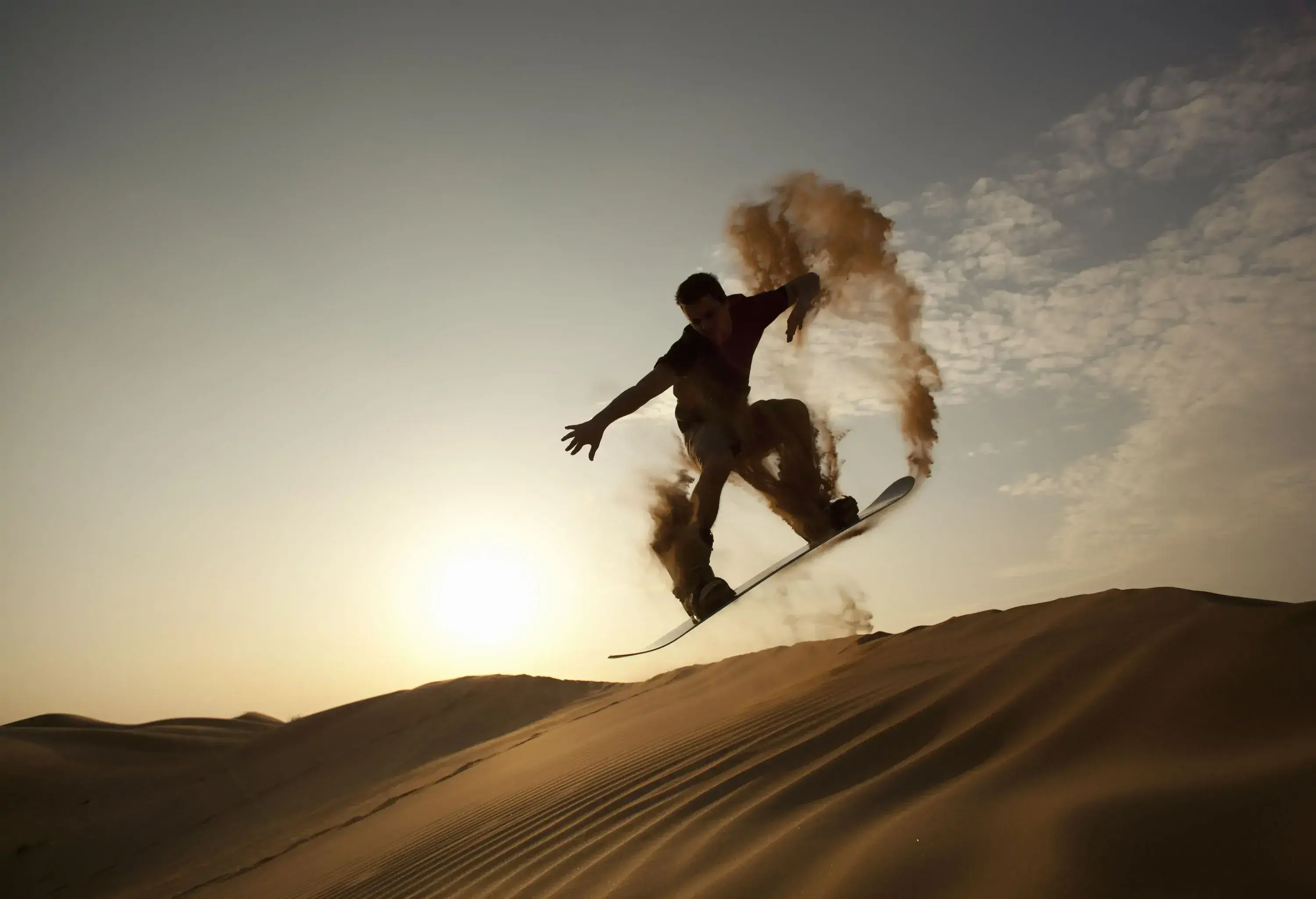 A man leaving a dust trail while riding a board down a sand dune.