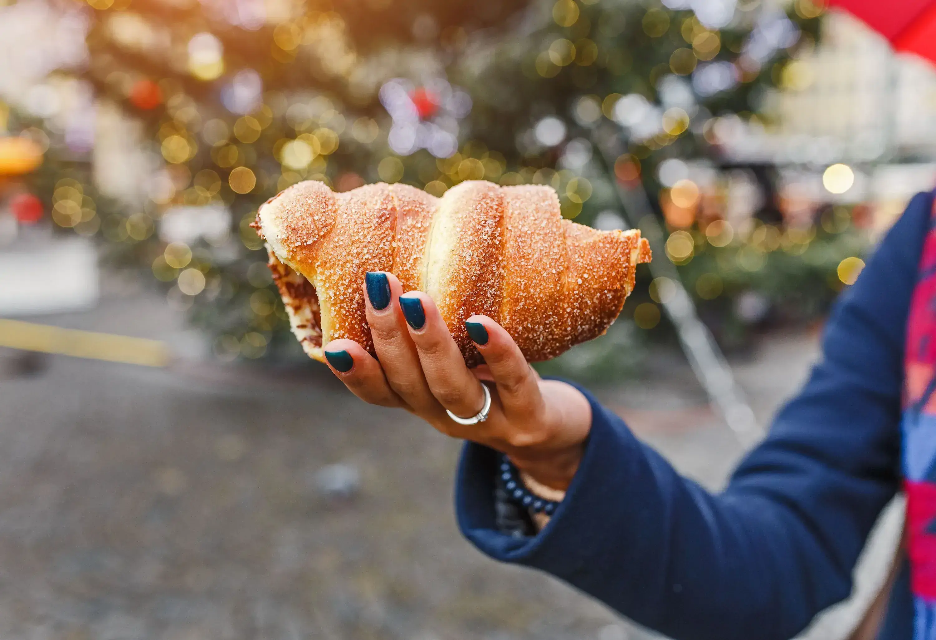 A hand with purple nails holding a sugar-sprinkled pastry roll.