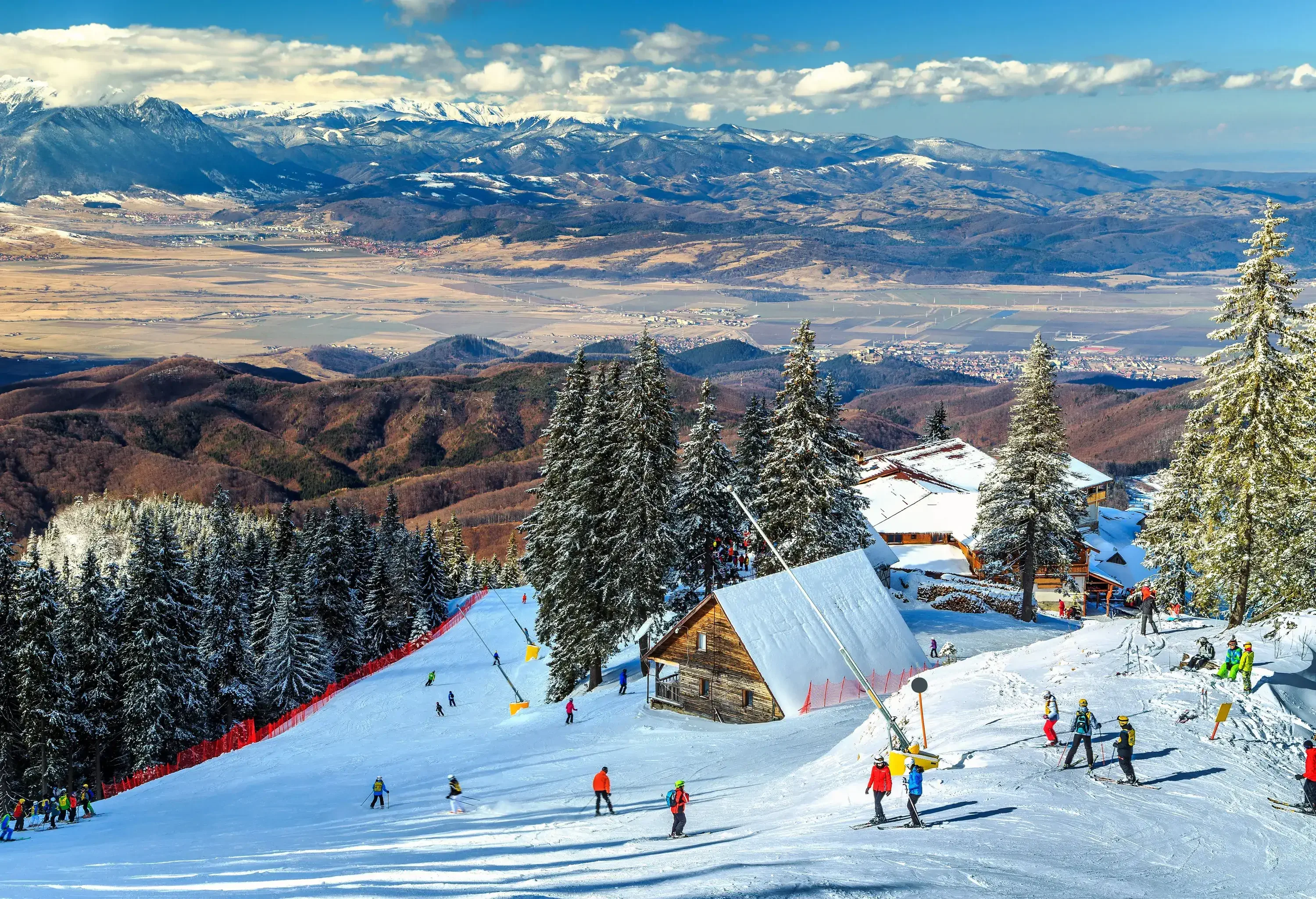 Wooden mountain cabins on a crowded snow hill next to frozen trees with distant mountain views.