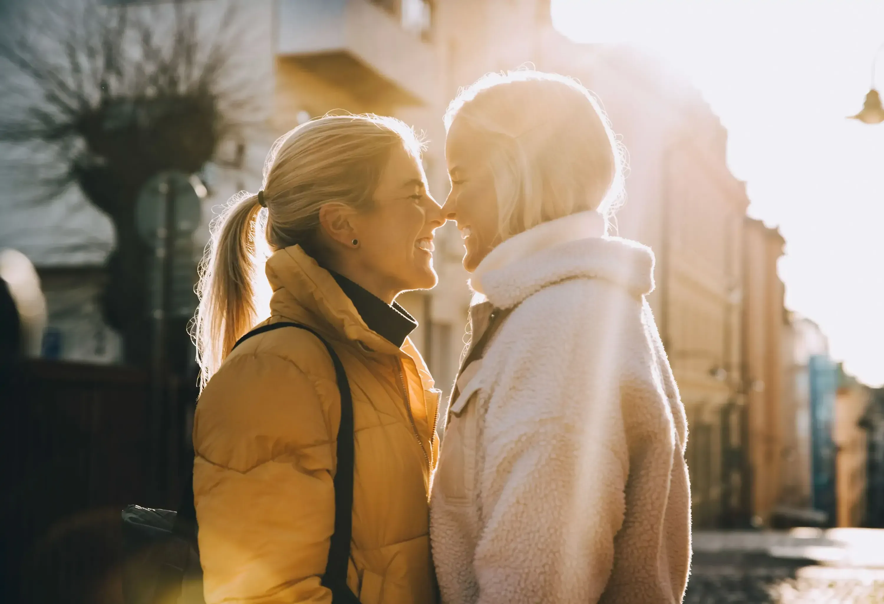 Two women in winter coats smiling and touching noses.