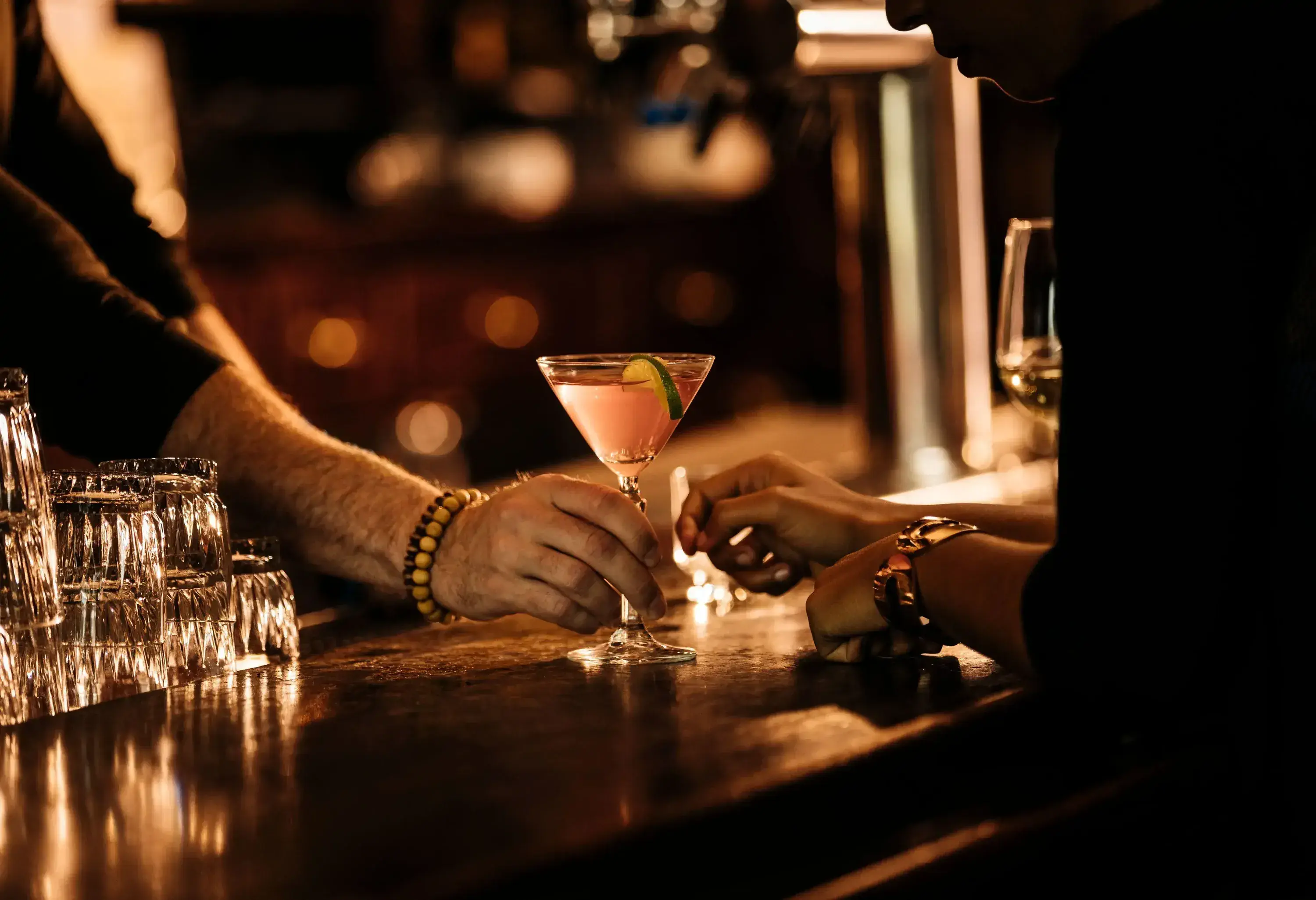 A bartender's hand serves a glass of drink to a customer in the bar.