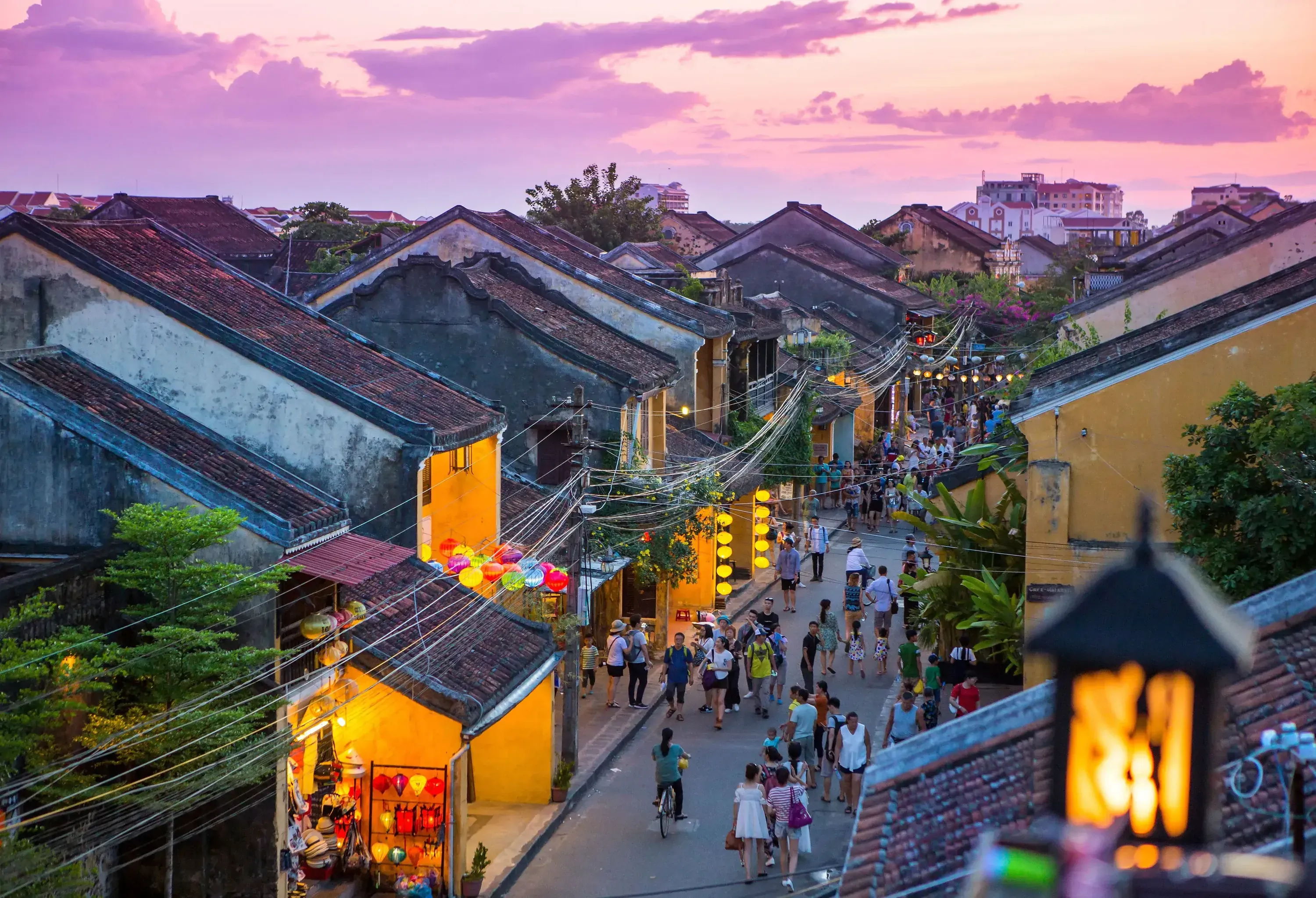 A lively street with people strolling along a charming thoroughfare, flanked by colourful houses adorned with paper lanterns, and an inviting array of shops and vendors along the way.
