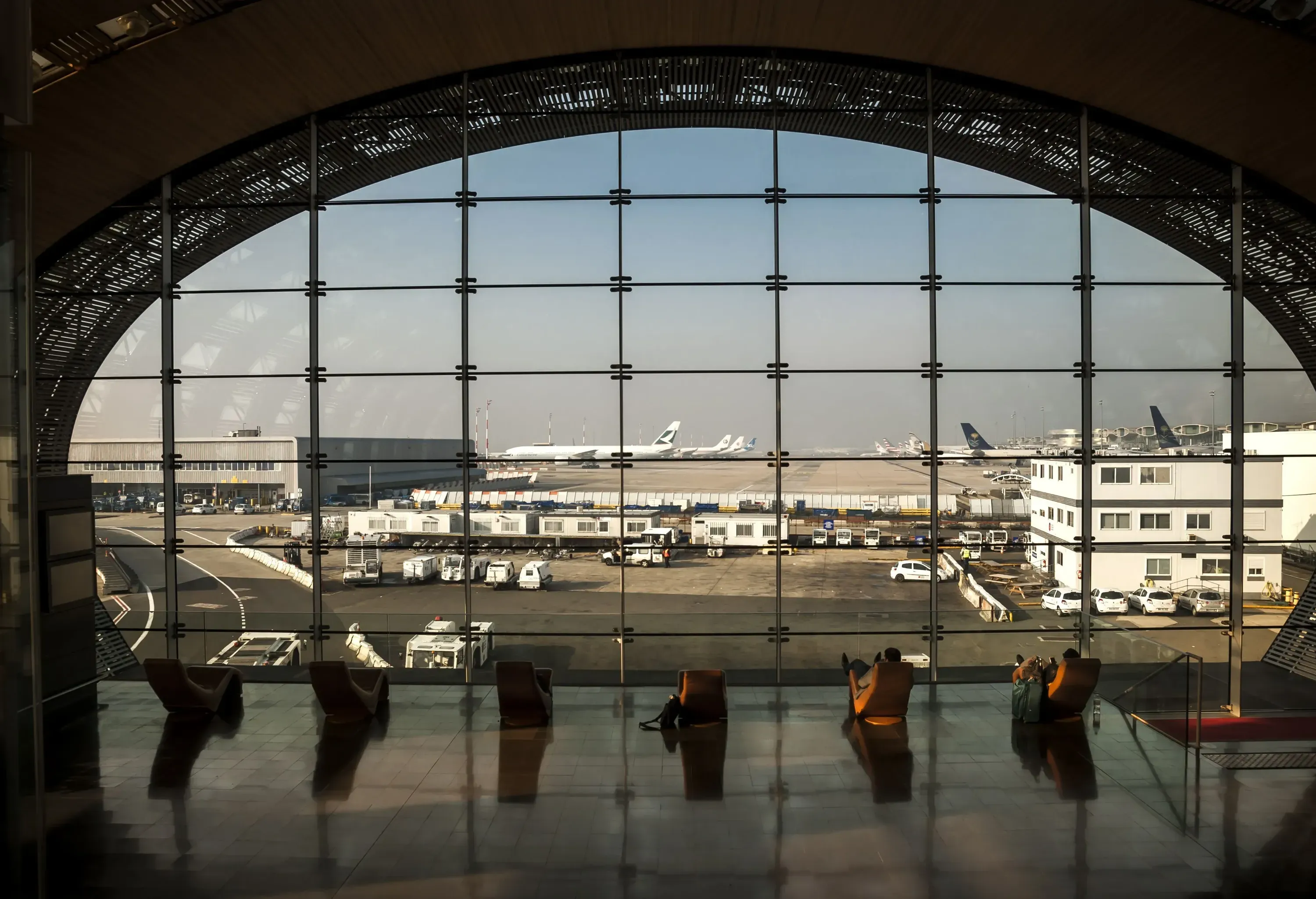 People sitting in loungers at an airport terminal overlooking the tarmac.