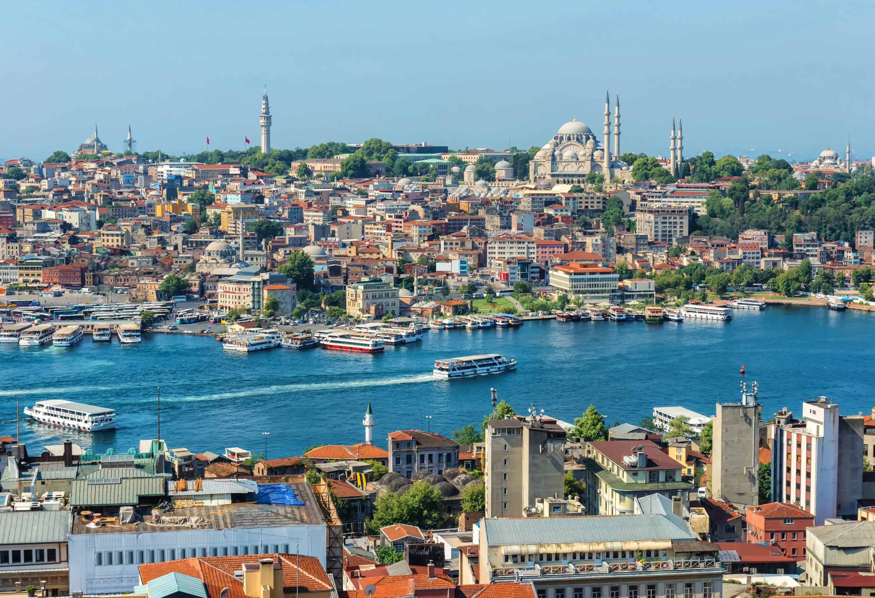 A ferry boat speeding along a waterway with historic structures lining its banks.