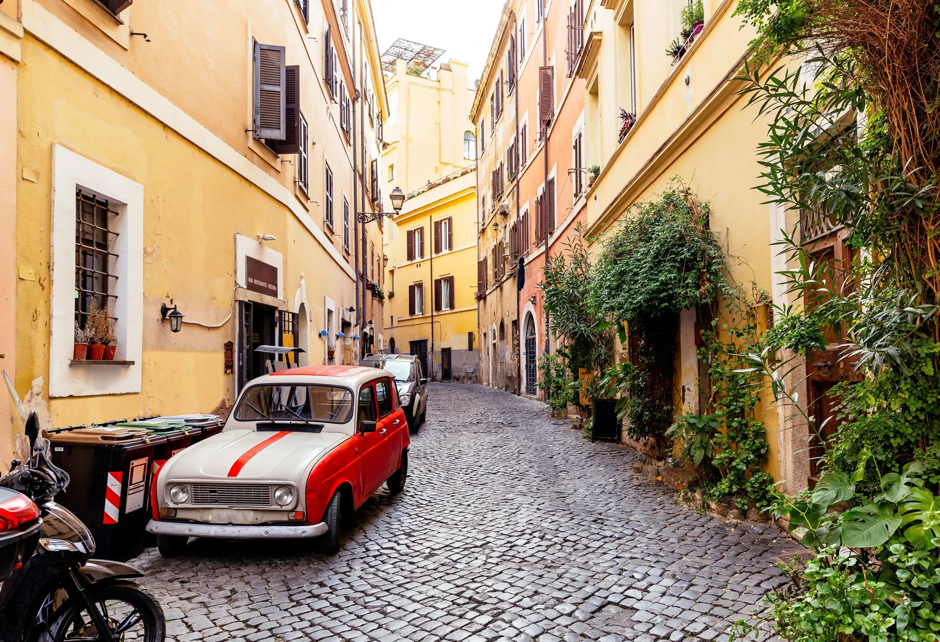 A brick-paved street with cars parked on the side and flanked by a row of buildings.