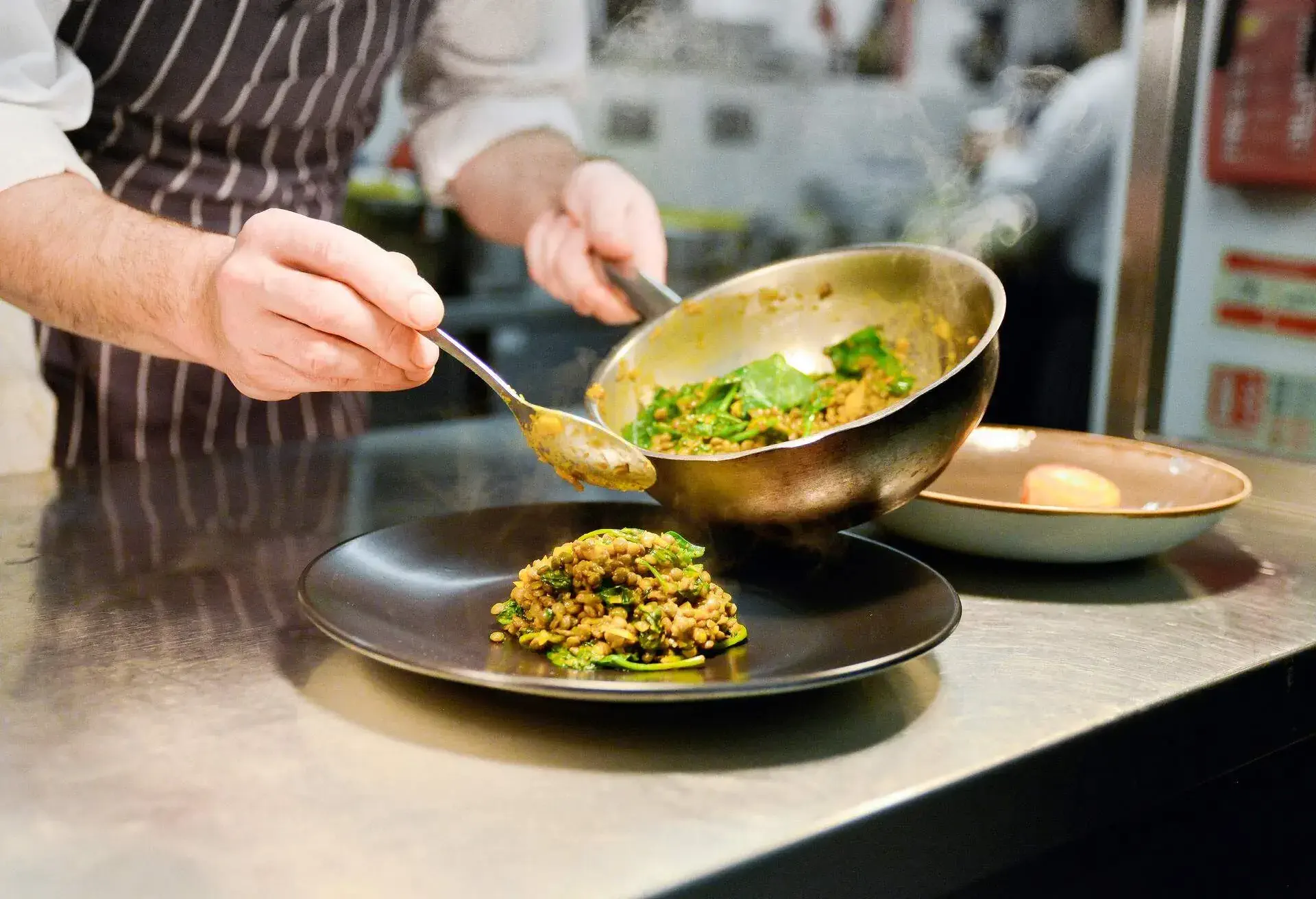 THEME_FOOD_RESTAURANT_KITCHEN_CHEF_PLACING_COOKED_LENTIL_DISH_GettyImages-674708451